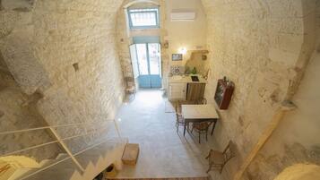 Ein Zimmer mit Steinwänden, einer Wendeltreppe, einer Essecke mit Tisch und Stühlen sowie einer Küchenzeile mit Spüle und Arbeitsfläche.