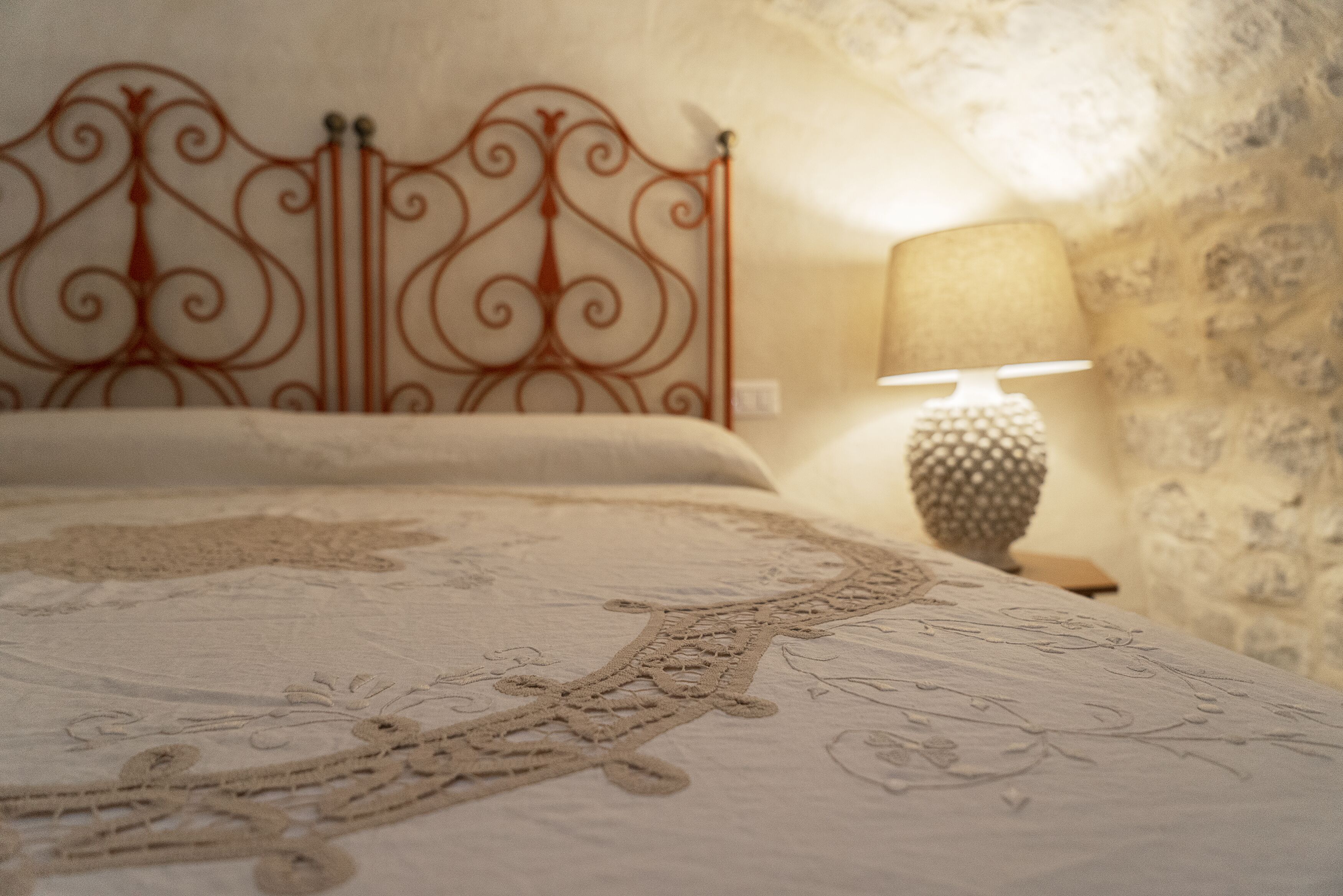 Un letto con una testiera in metallo decorata, una parete dalla texture particolare e una lampada su un comodino.