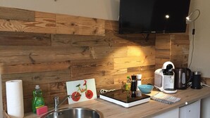 Une cuisine moderne avec un revêtement mural en bois, un évier en acier inoxydable, une machine à café et un téléviseur à écran plat fixé au mur.