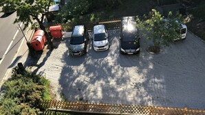 Un espace de stationnement avec plusieurs voitures, une benne à ordures rouge et une clôture en bois.