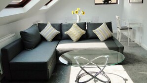 A modern living room with a sectional sofa, a glass coffee table, and a skylight above.