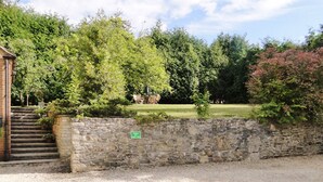 A stone wall with a parking sign, a gravel area, and a grassy field with trees in the background.