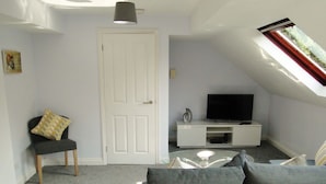 A living room with a grey sofa, a small black chair, a white entertainment unit, and a television.