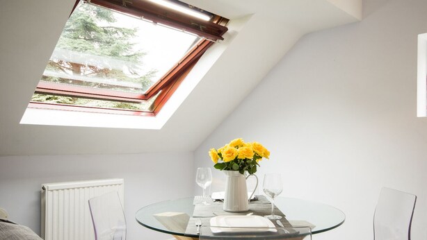 A modern dining area with a glass table, white cushions, and a vase of yellow flowers.