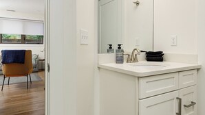 A modern bathroom with a large mirror, white cabinetry, and a wooden floor. - Downtown Escape 1BR Condo (Traverse City)