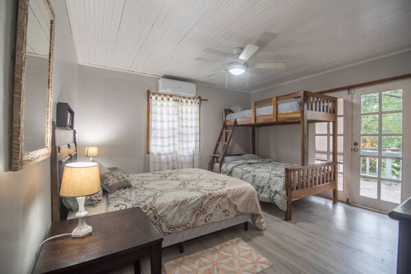 Un dormitorio con dos camas, un ventilador de techo, una ventana con cortinas y una puerta que da al exterior.
