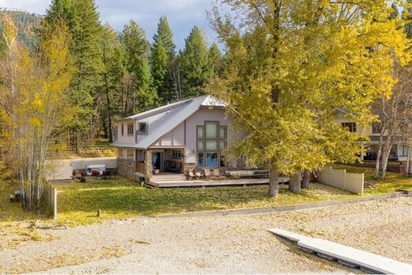 A single-story house with a front porch, surrounded by trees and a gravel driveway.