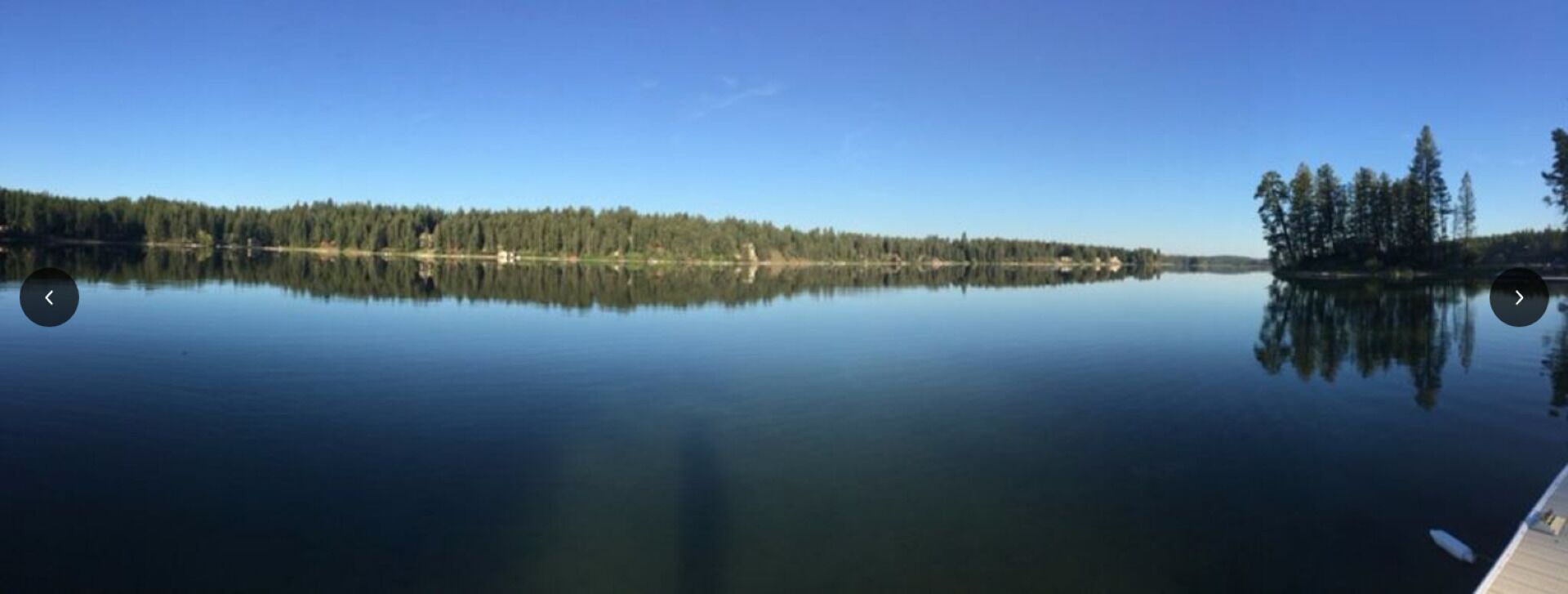 Tyyni järvi, jonka oikealla puolella on laituri, ja järveä ympäröi tiheä metsä.