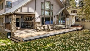 A two-story house with a covered patio, stone pillars, and a large deck area. - Lake House on Lake Blaine (Kalispell)