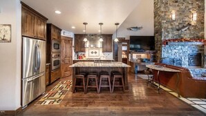 A spacious kitchen with a large island, wooden cabinets, stainless steel appliances, and a stone fireplace. - Lake House on Lake Blaine (Kalispell)