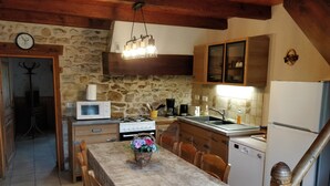 Une cuisine rustique avec un mur en pierre, des armoires en bois, un poêle blanc et une table à manger avec des chaises.