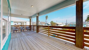 Une terrasse en bois avec une rambarde, des sièges d’extérieur et une vue sur des maisons et des palmiers.