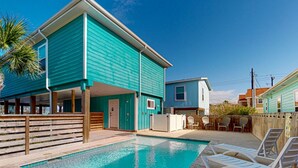 Un bâtiment turquoise doté d’une piscine et de chaises longues.
