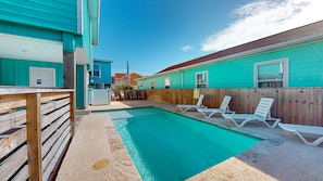 A swimming pool with lounge chairs, a wooden deck, and a wooden fence.