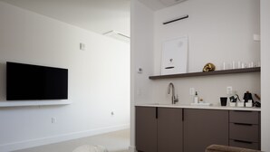 Ein modernes Wohnzimmer mit Flachbildfernseher, einer Couch, einem Couchtisch und einer Küchenzeile mit Spüle und Schränken.