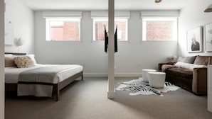 A bedroom with a bed, a sofa, a zebra rug, and a brick wall visible through the windows. - Boutique Hotel Room above The Jefferson Theater on the Downtown Mall (Charlottesville)