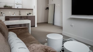 A modern living room with a sofa, a coffee table, a flat-screen TV mounted on the wall, a small white table, and a mirror. - Boutique Hotel Room above The Jefferson Theater on the Downtown Mall (Charlottesville)