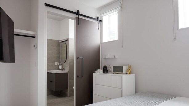 Une chambre moderne comprenant un lit, une commode, une coiffeuse avec un miroir et une porte coulissante donnant accès à une salle de bain.