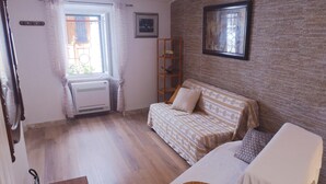 Una habitación con piso de madera, un sofá con ropa de cama estampada, una mesita y un radiador.