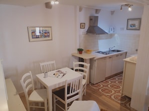 Una cocina compacta con armarios blancos, una pequeña mesa de comedor con sillas, un lavamanos y una estufa.