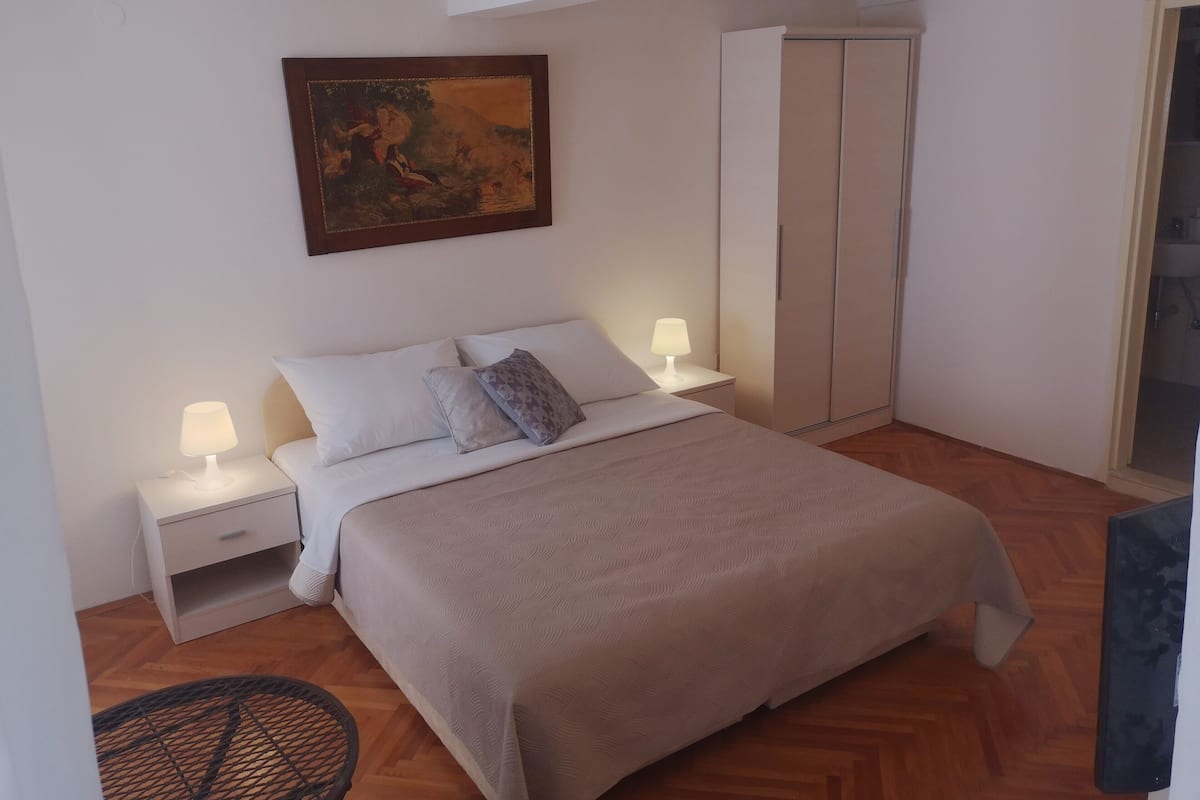 A bedroom with a bed, nightstands, a lamp, a wardrobe, and a painting on the wall.