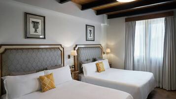 A hotel room with two beds, a large window with curtains, and framed artwork on the walls.