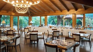Un comedor espacioso con vigas de madera, ventanas amplias y una araña. Las mesas están dispuestas para comer, y hay sillas alrededor.