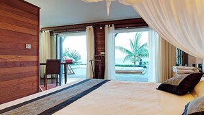 Een slaapkamer met een groot bed, een bureau en uitzicht op palmbomen en de oceaan.