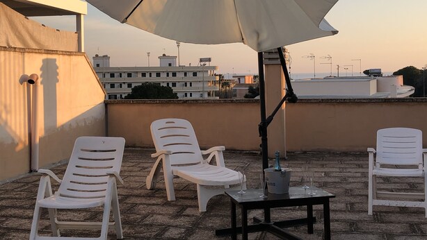 Een terras op het dak met witte plastic stoelen, een tafel en een grote parasol.