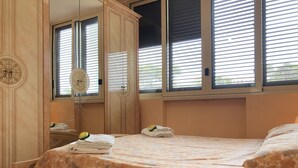 Een slaapkamer met een bed, een spiegel en een raam met jaloezieën.