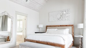A bedroom with a wooden bed, white bedding, a bench, a mirror, and a decorative wall piece. - Private Pool | Walk to Rosemary Beach (Panama City Beach)