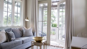 A cozy living room with a grey sofa, a bowl on a small table, and large windows with curtains. - Carriage House | Walk to Dining and Beach (Panama City Beach)