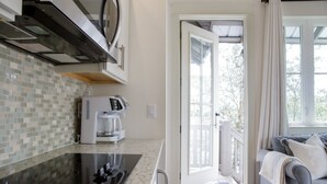 A kitchen with a coffee maker, a stove, and a tiled backsplash. There is a door leading to a balcony with a view of trees. - Carriage House | Walk to Dining and Beach (Panama City Beach)