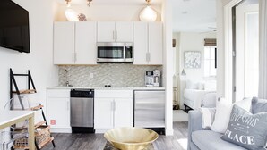 A modern kitchen with white cabinets, a microwave, and a coffee machine. There is a gray sofa with a pillow that says "LOVE THIS PLACE". - Carriage House | Walk to Dining and Beach (Panama City Beach)