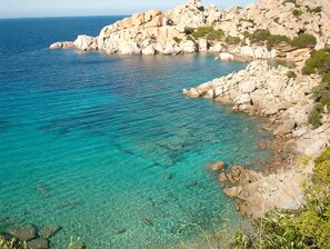A coastal landscape with clear turquoise waters, rocky terrain, and sparse vegetation.