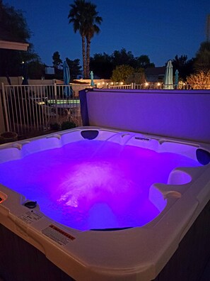 Un jacuzzi con luz púrpura, rodeado por una valla y palmeras.