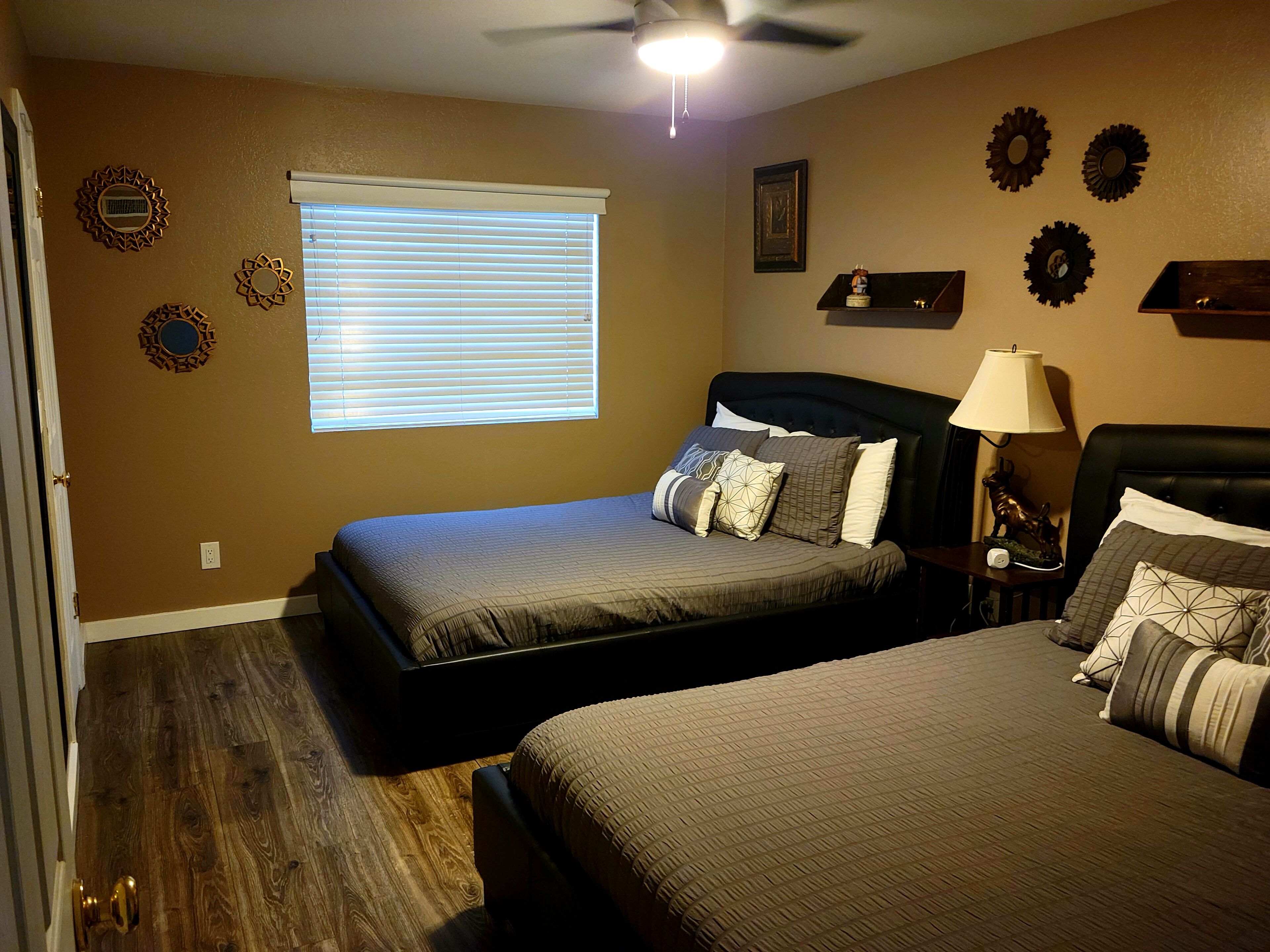 Une chambre avec deux lits, un ventilateur de plafond, une fenêtre avec des stores et des décorations murales.