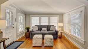 A living room with a sofa, two ottomans, a small table, and a lamp. - Oyster Shell Cottage (St Simons Island)