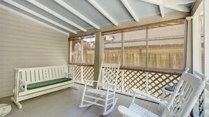 A covered porch with a white bench, rocking chairs, and a lattice screen. - Oyster Shell Cottage (St Simons Island)