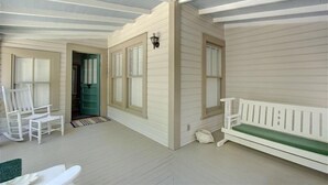 A covered porch with a bench, chairs, and a door leading to an interior space. - Oyster Shell Cottage (St Simons Island)