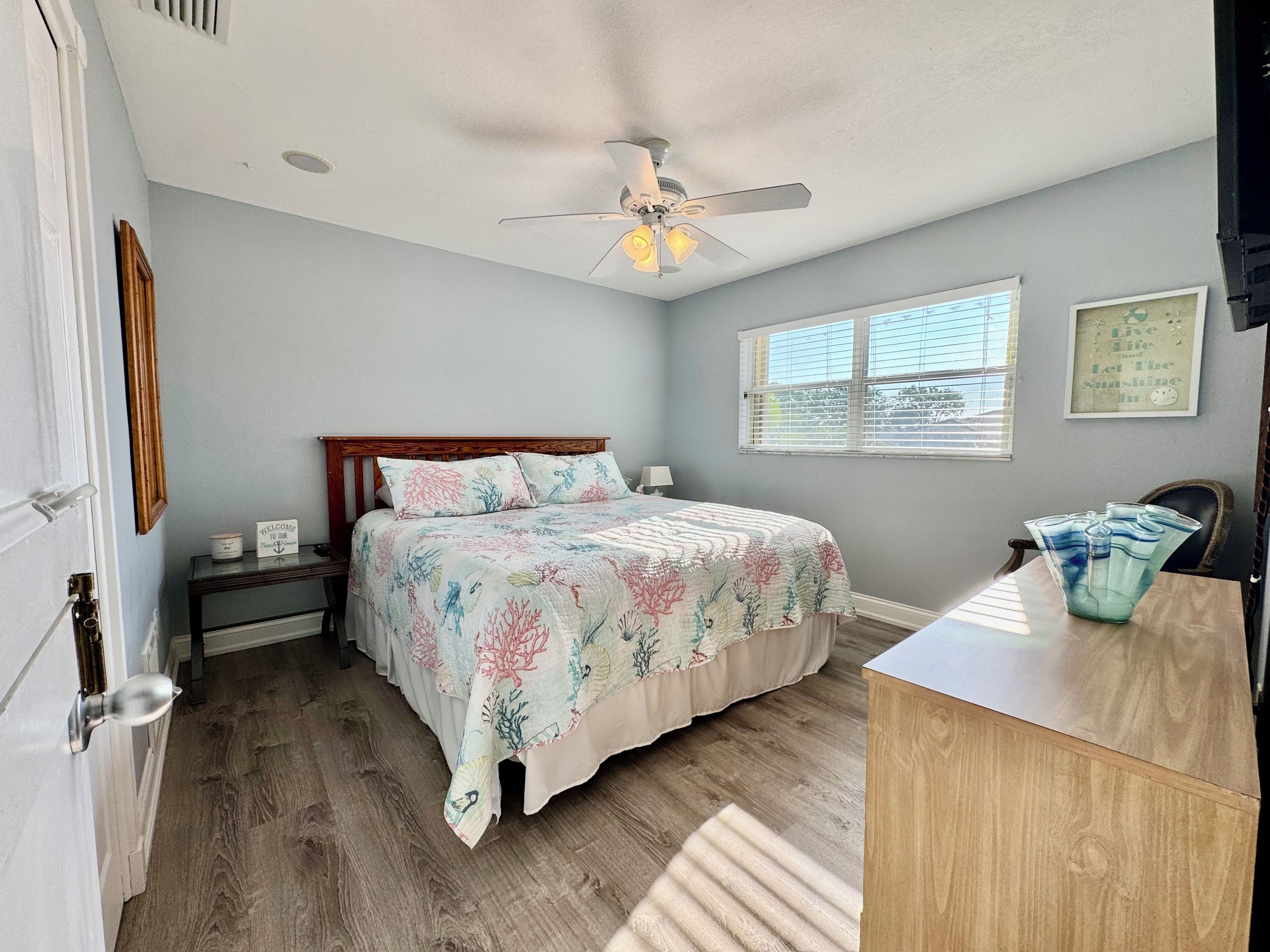 A bedroom with a bed, a ceiling fan, a window, a bedside table, and a dresser.
