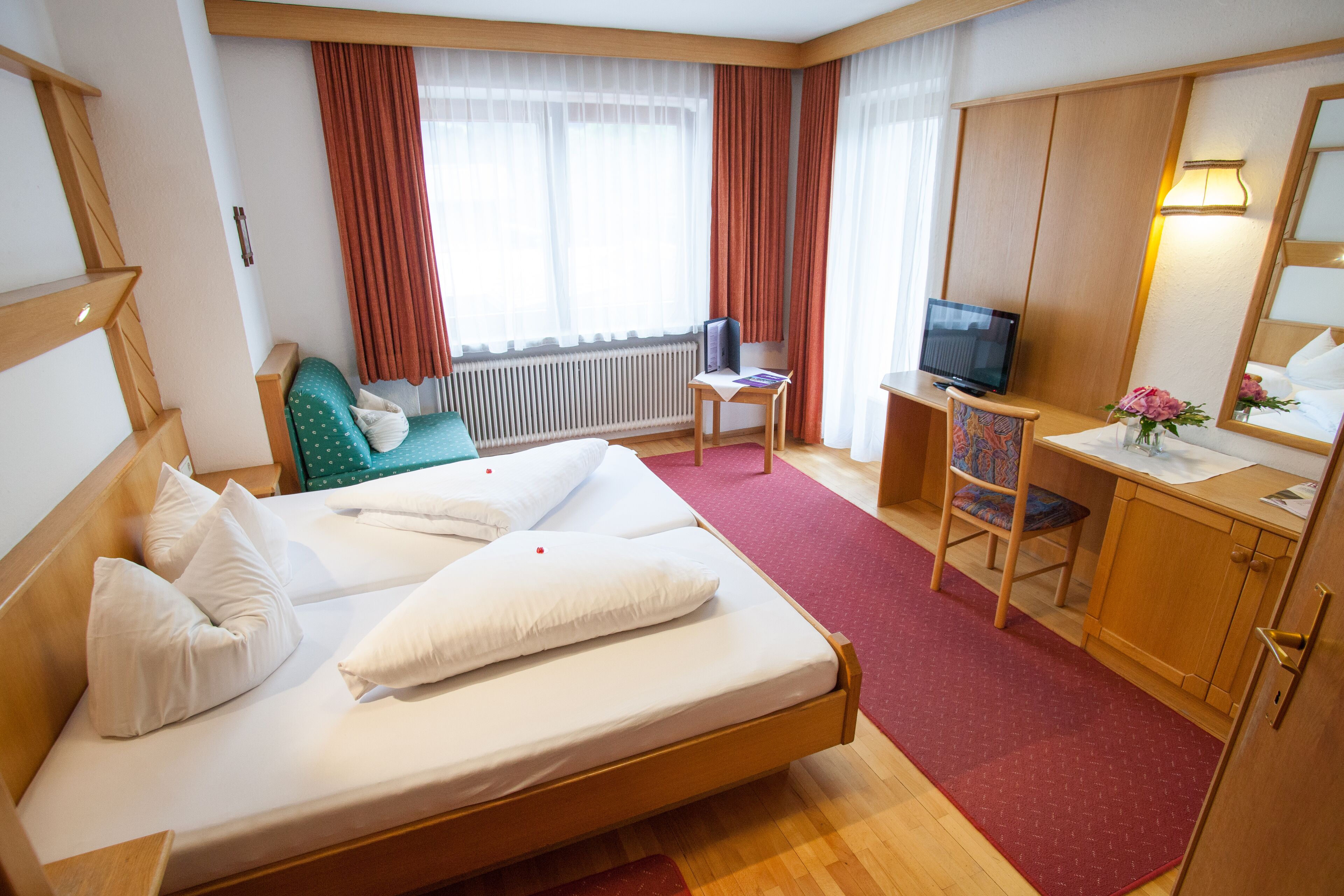 A hotel room with a bed, a desk with a chair, a television, and a window with curtains.
