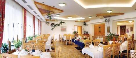 A spacious dining area with multiple tables and chairs, featuring a tiled floor and ceiling with recessed lighting.