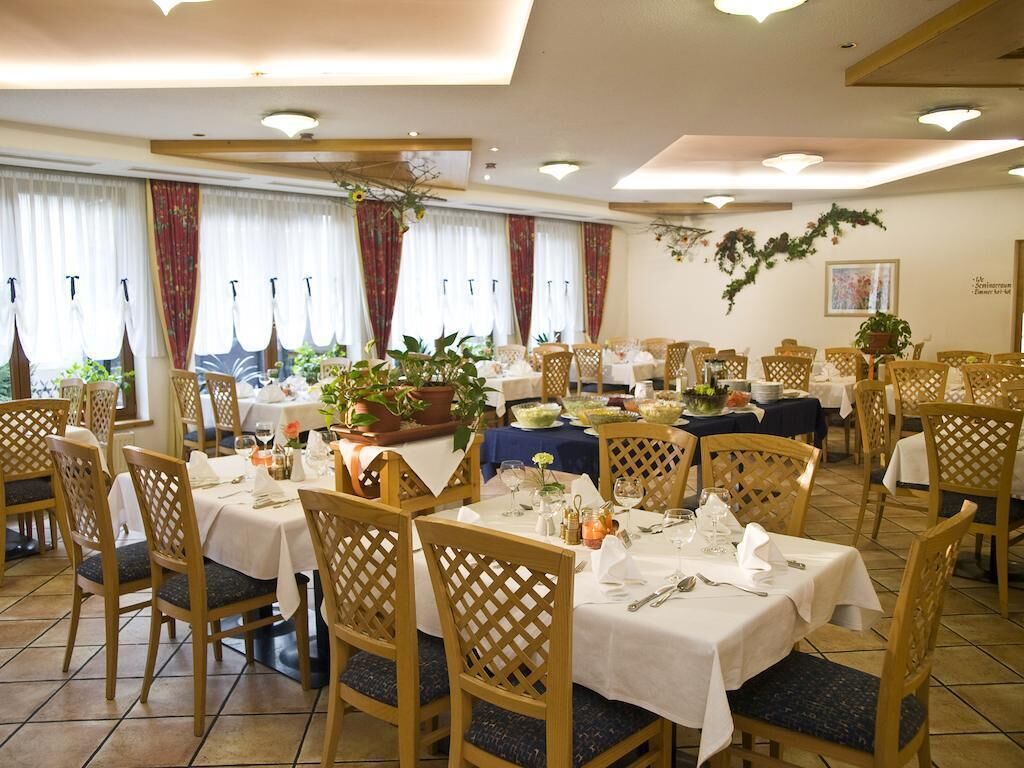 A dining area with multiple tables and chairs, each set with white tablecloths and silverware.