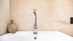 Een badkamer met een witte badkuip, een chromen kraan en een decoratieve fles met reliëf links.
