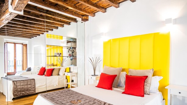 Een moderne hotelkamer met een groot bed, een geel accentmuur en houten balken aan het plafond.