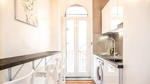 Een compacte keuken met een wasmachine, een spoelbak en een eethoek met witte stoelen.