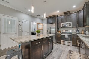 A modern kitchen with dark wood cabinets, stainless steel appliances, and a granite countertop. - Vacation Homes at Buckroe Beach! Sleeps 10 (Hampton)