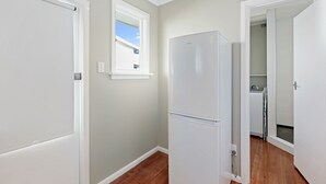 A kitchen with a white refrigerator, wooden flooring, and a window with a view of the sky.