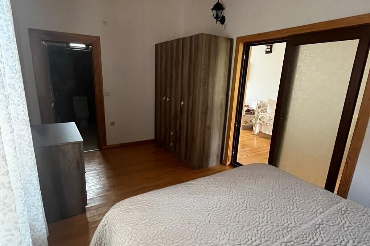 Un dormitorio con una cama, un armario, una puerta que da a otra habitación y una lámpara en el techo.